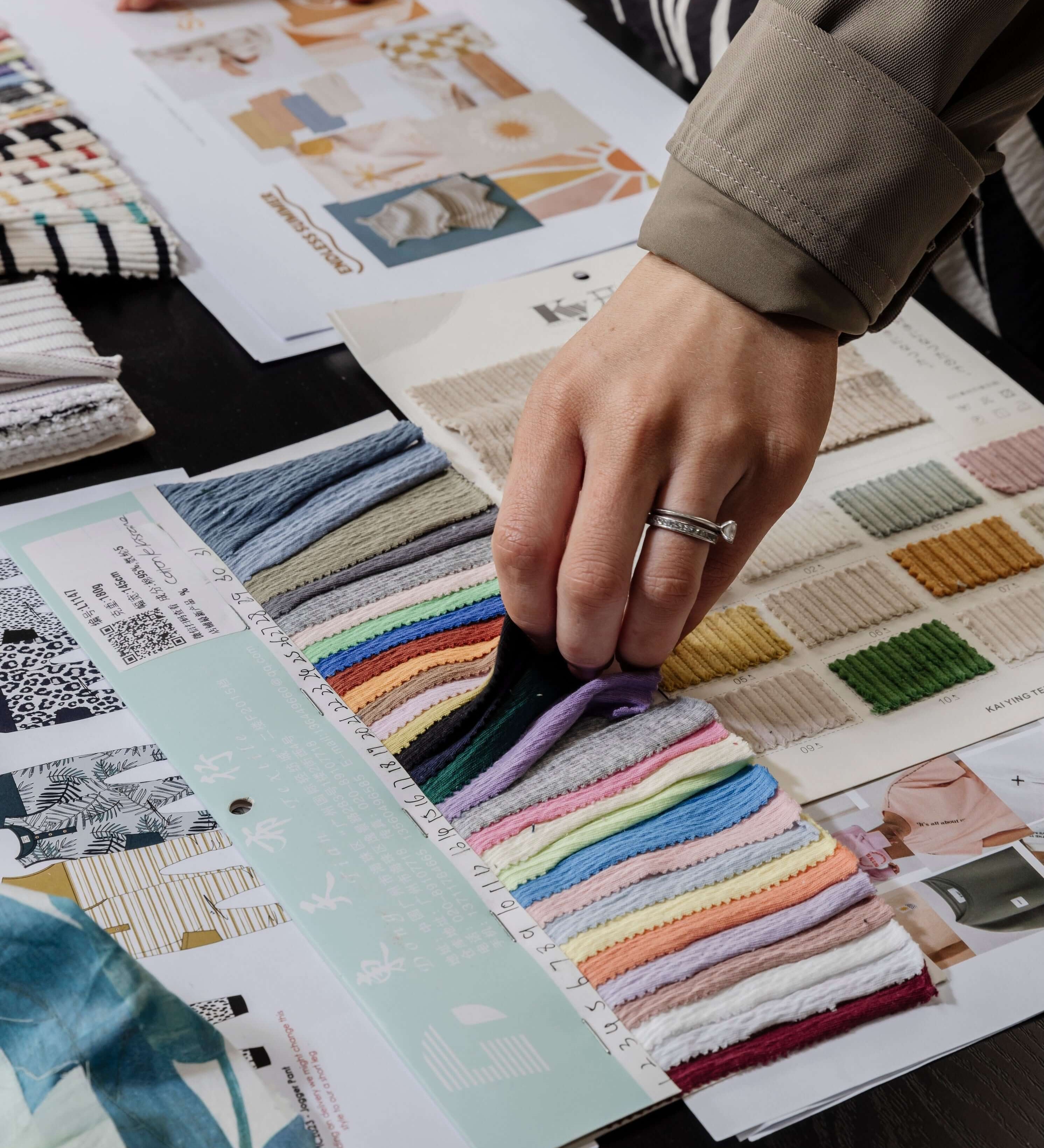 The hands of a lady choosing the colour fabric for her fashion brand from material swatches