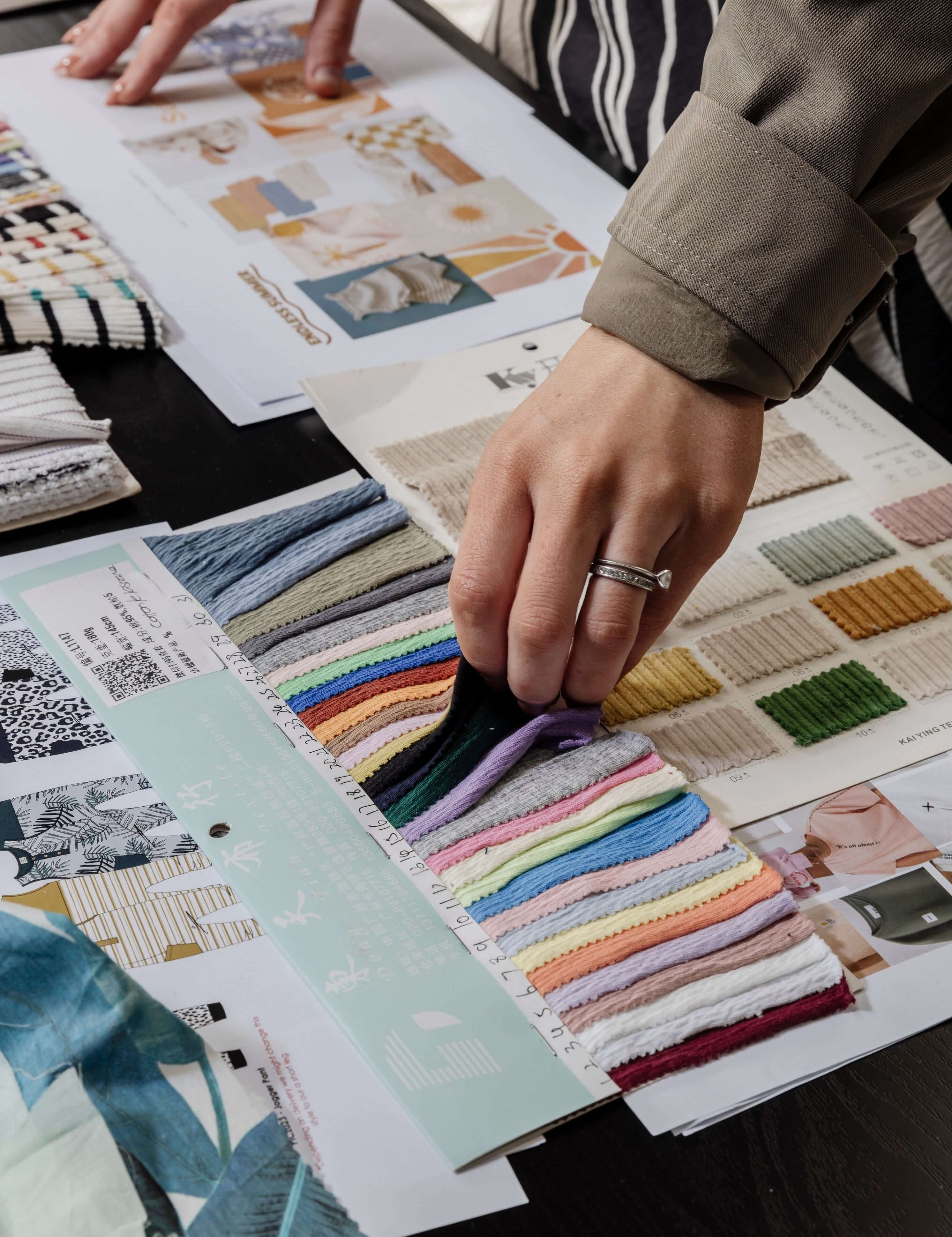 The hands of a lady choosing the colour fabric for her fashion brand from material swatches