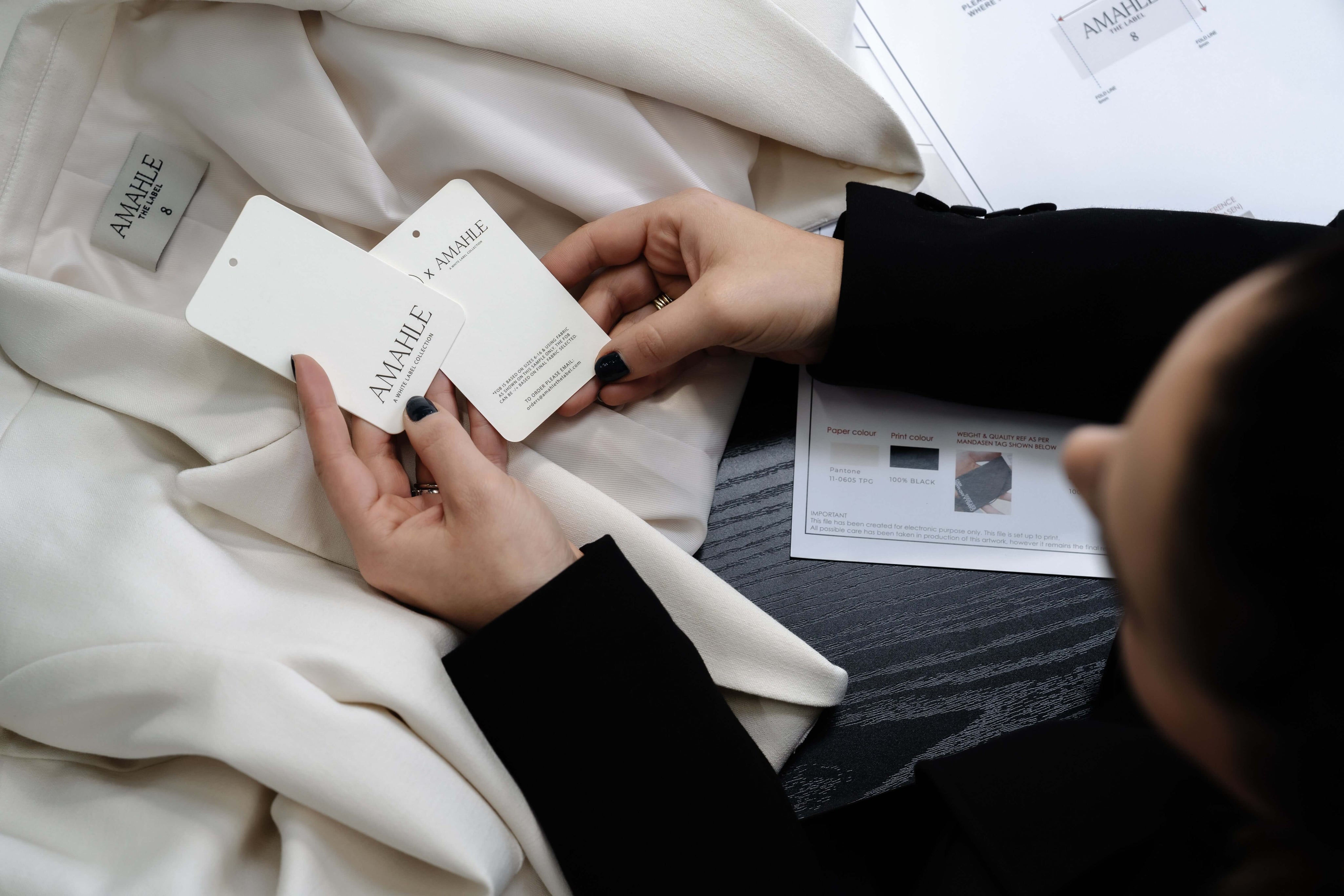The hands of a lady holding her hangtag and woven label up to her sample garment.