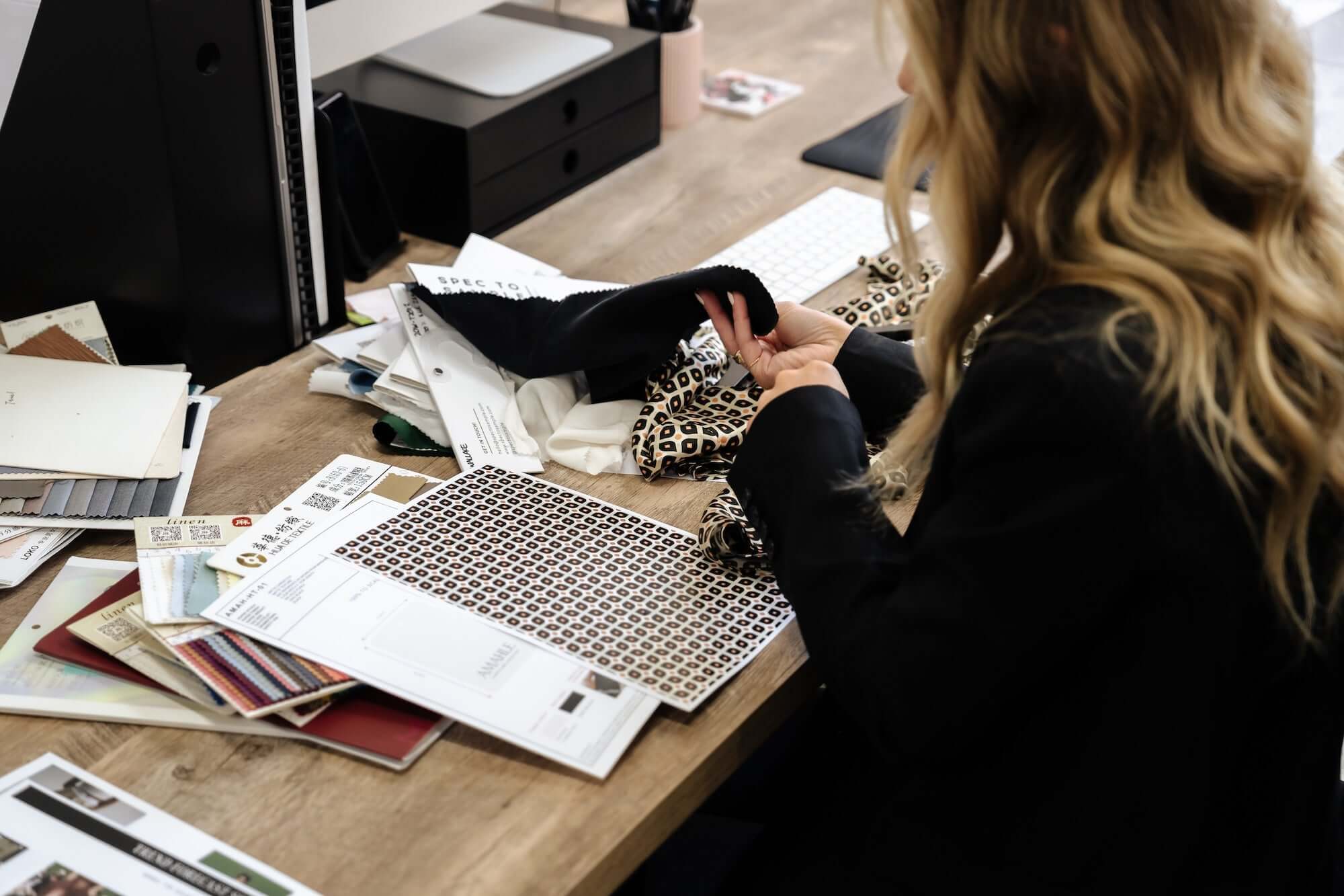 Fashion designer working at desk reviewing product development tech pack.